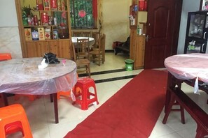 A room with a red carpet, wooden furniture, a dining table with a plastic cover, and a cabinet with various items. - nqkz (Wuyuan)