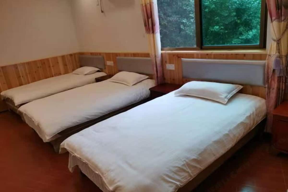 A room with two single beds, wooden walls, a window with curtains, and a radiator.