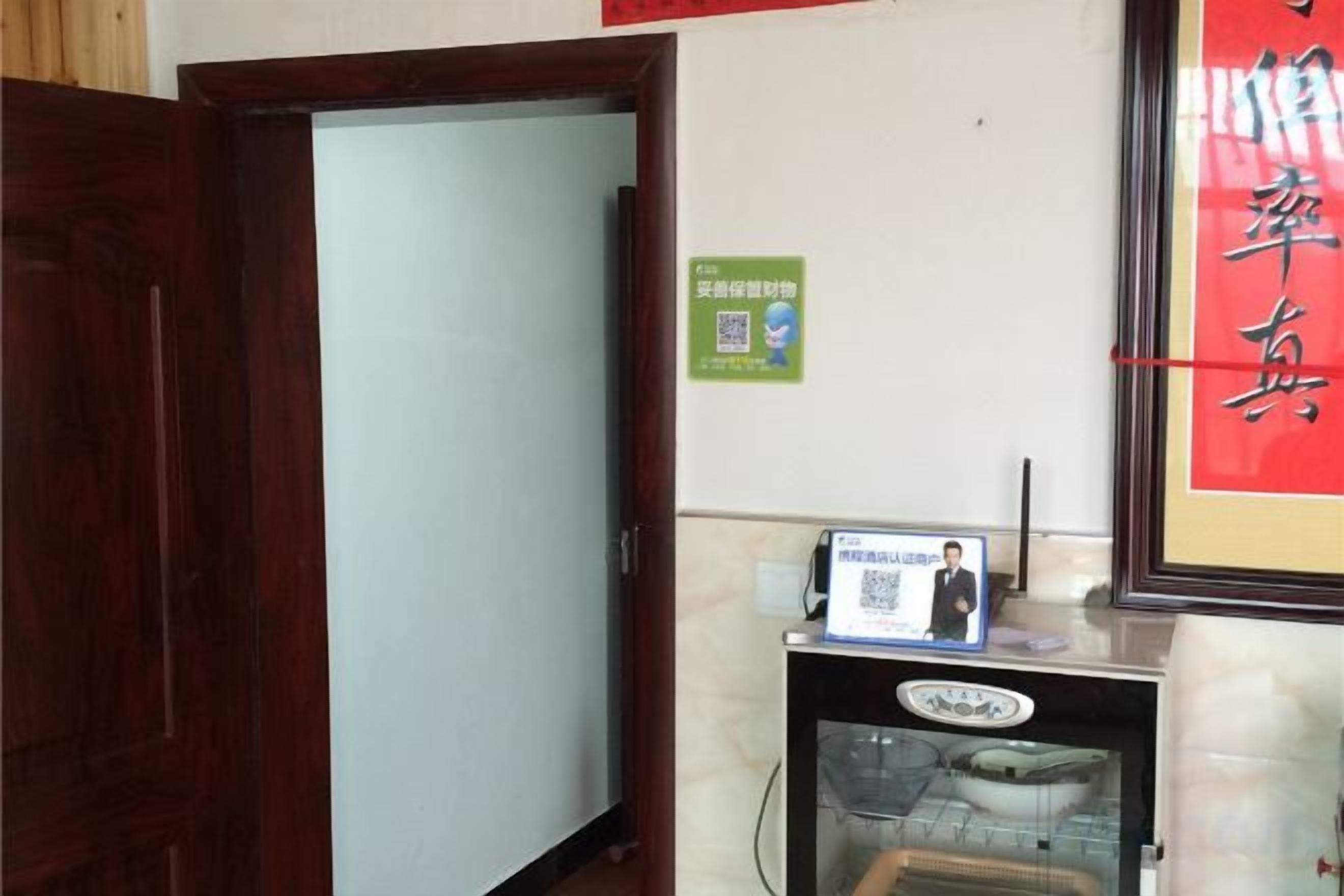 A hotel room with a wooden door, a glass door, a small refrigerator, and a wall-mounted shelf with a framed picture.