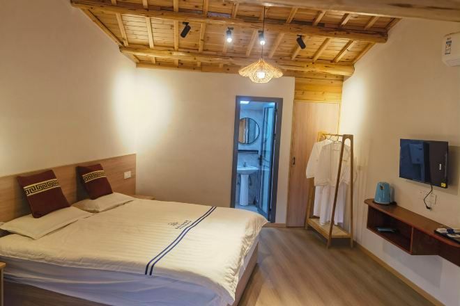 A bedroom with a wooden ceiling, a bed with a headboard, a mirror, a television, and a small shelf.