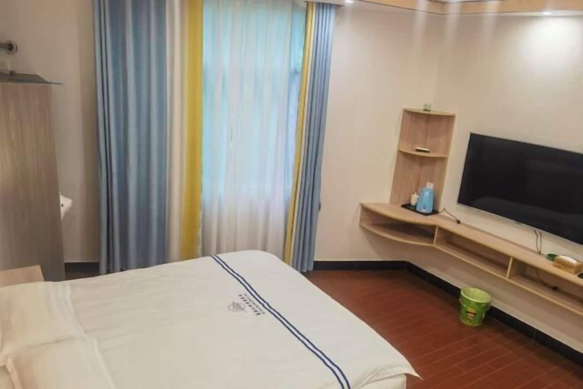 A hotel room with a bed, a television, a small shelf with toiletries, and a curtain.