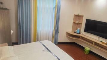 Een hotelkamer met een bed, een televisie, een klein plankje met toiletartikelen en een gordijn.