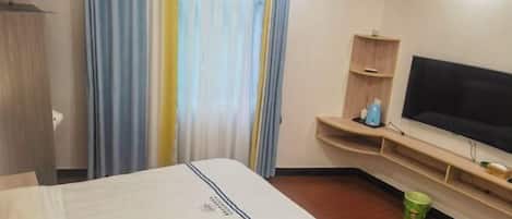 Habitación de hotel con cama, televisor, un estante pequeño con artículos de aseo y cortina.