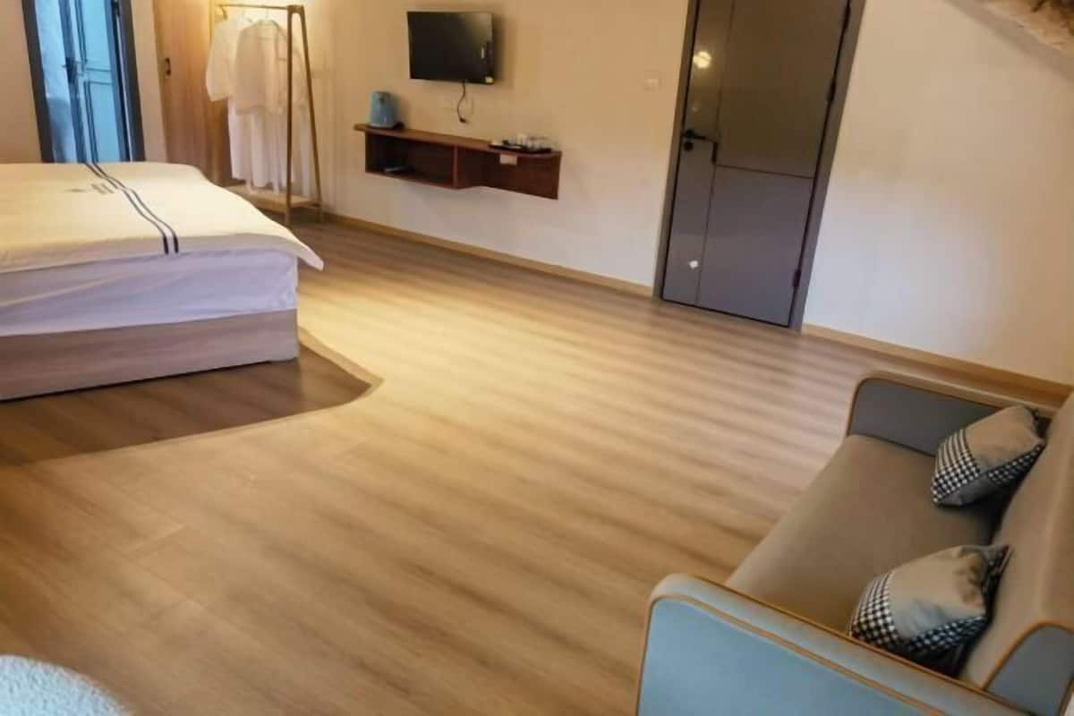 A hotel room with a bed, a sofa, a TV mounted on the wall, and a clothing rack.