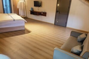 A hotel room with a bed, a sofa, a TV mounted on the wall, and a clothing rack. - nqkz (Wuyuan)