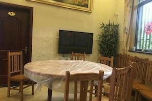 Un salón de conferencias con una mesa redonda, sillas de madera, un televisor y una planta en maceta.