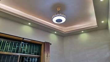 Een kamer met plafondventilator, inbouwverlichting en een raam met zonwering.