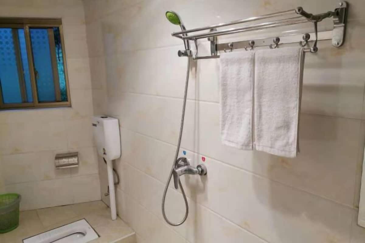 A bathroom with a shower, a toilet, a hand dryer, and a window with blinds.