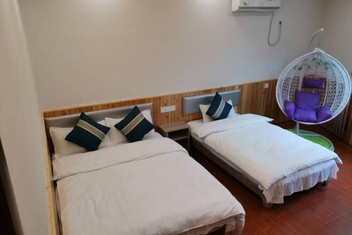 Two single beds with white linens and dark pillows, a hanging chair, and a wooden headboard.