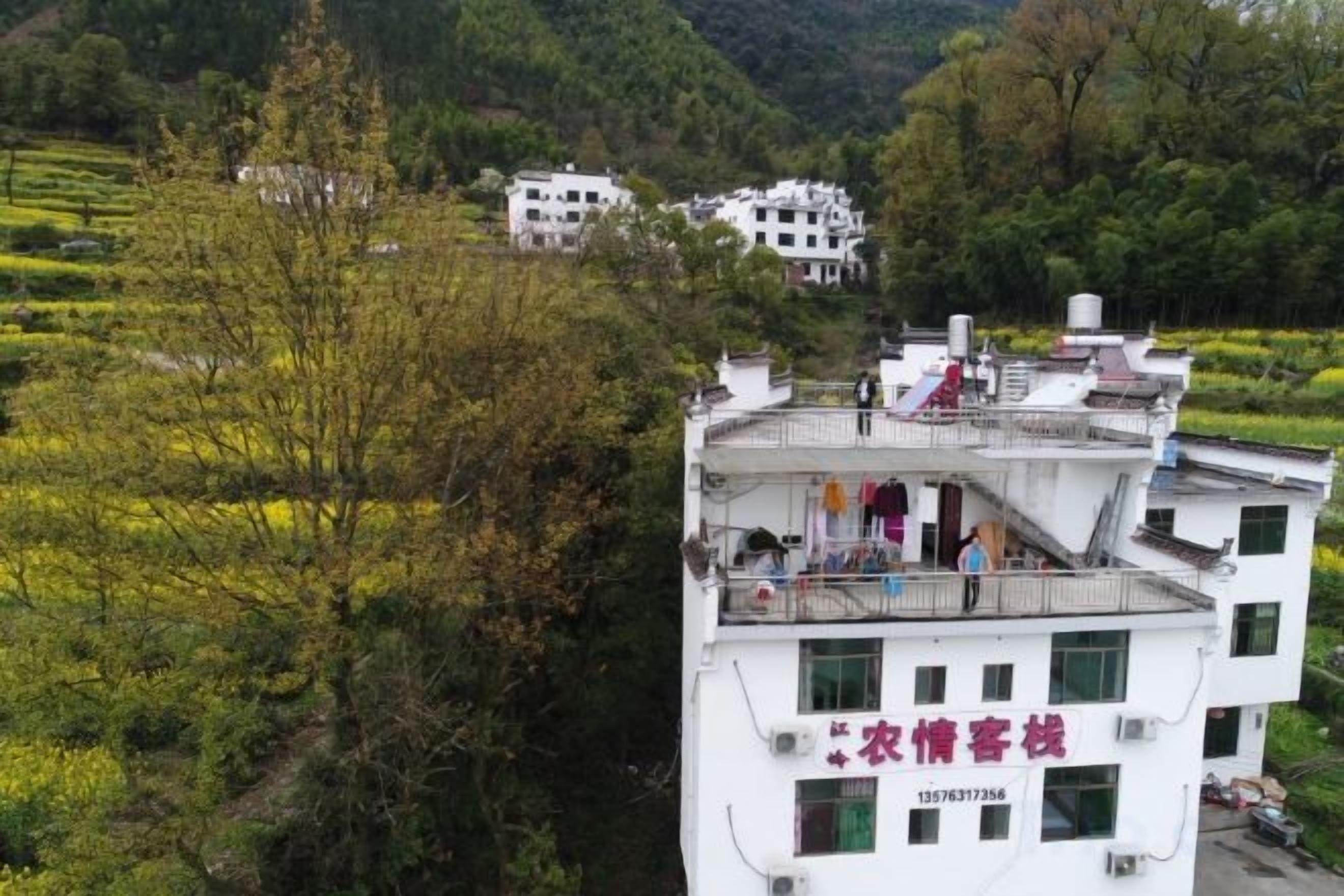 A multi-story building with balconies, surrounded by greenery and hills.