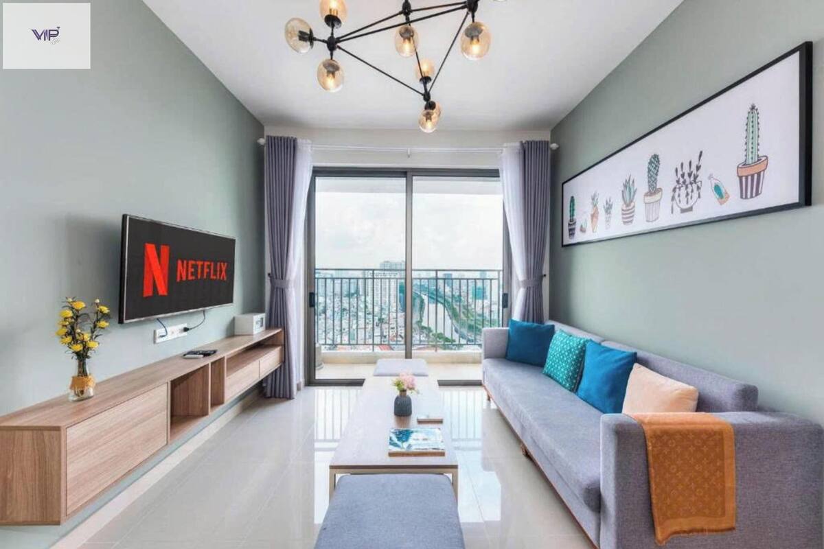 A modern living room with a flat-screen TV, a sofa, a coffee table, and a large window with a balcony view.