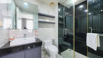 A modern bathroom with a glass-enclosed shower, a white toilet, and a vanity with a mirror and countertop.