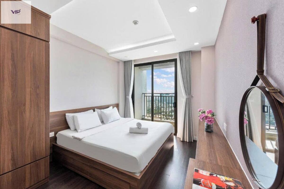 A hotel room with a large bed, a wooden wardrobe, a round mirror, and a balcony with a view.