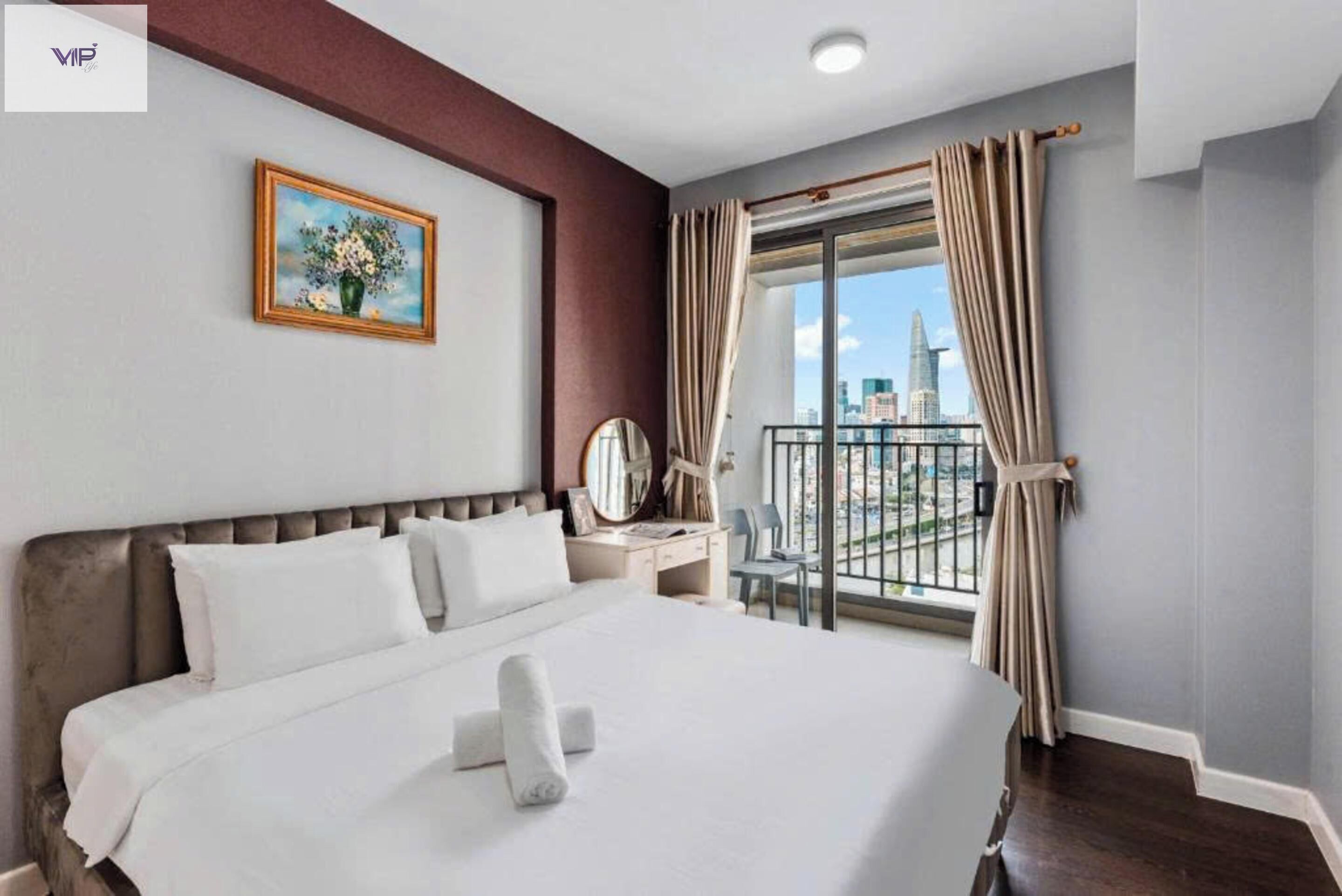 A hotel room with a large bed, a bedside table, a mirror, and a view of the city through a balcony.