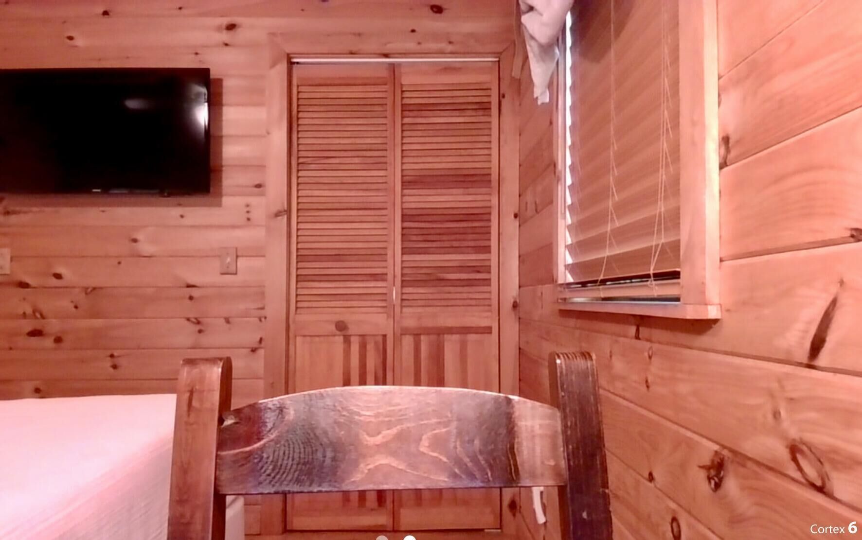 Een blokhut met een bed, een houten stoel, een televisie en een raam met jaloezieën.
