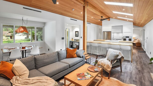 Un salon moderne avec un canapé gris, une table basse en bois et un coin repas comprenant une table et des chaises en bois.