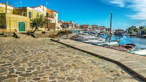 A stone-paved waterfront with boats docked and buildings along the shore. - Dimora Oleandro 50mt From Beach (Stintino)