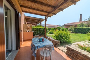 An outdoor patio with a table set for two, a covered seating area, and a view of a garden and house in the background. - Dimora Oleandro 50mt From Beach (Stintino)