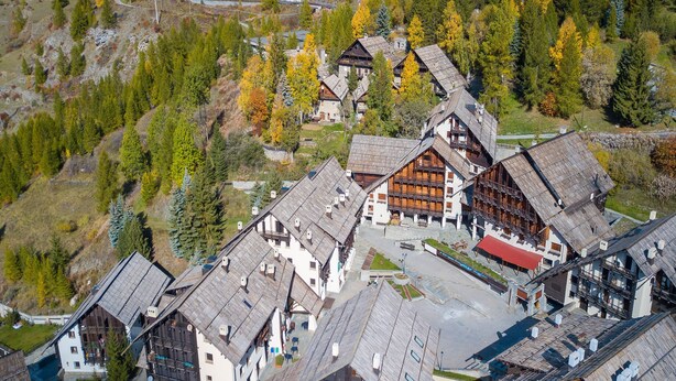 Il s’agit d’un bâtiment traditionnel de style chalet, en bois, doté d’un toit à forte pente et entouré d’une zone boisée aux couleurs automnales.