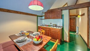 Un coin repas avec une table en bois dressée pour quatre personnes, un saladier de fruits et une suspension lumineuse.