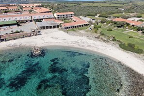 Oversigtsbillede af et kysthotel med flere bygninger, en sandstrand og klart, blåt vand.