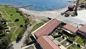 Ett flygbildsfoto av en fastighet vid kusten med en strand, en stor byggnad med ett rött tak och en skorsten.