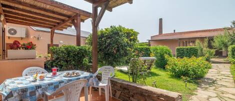 An outdoor patio with a table and chairs, surrounded by a stone wall and greenery.