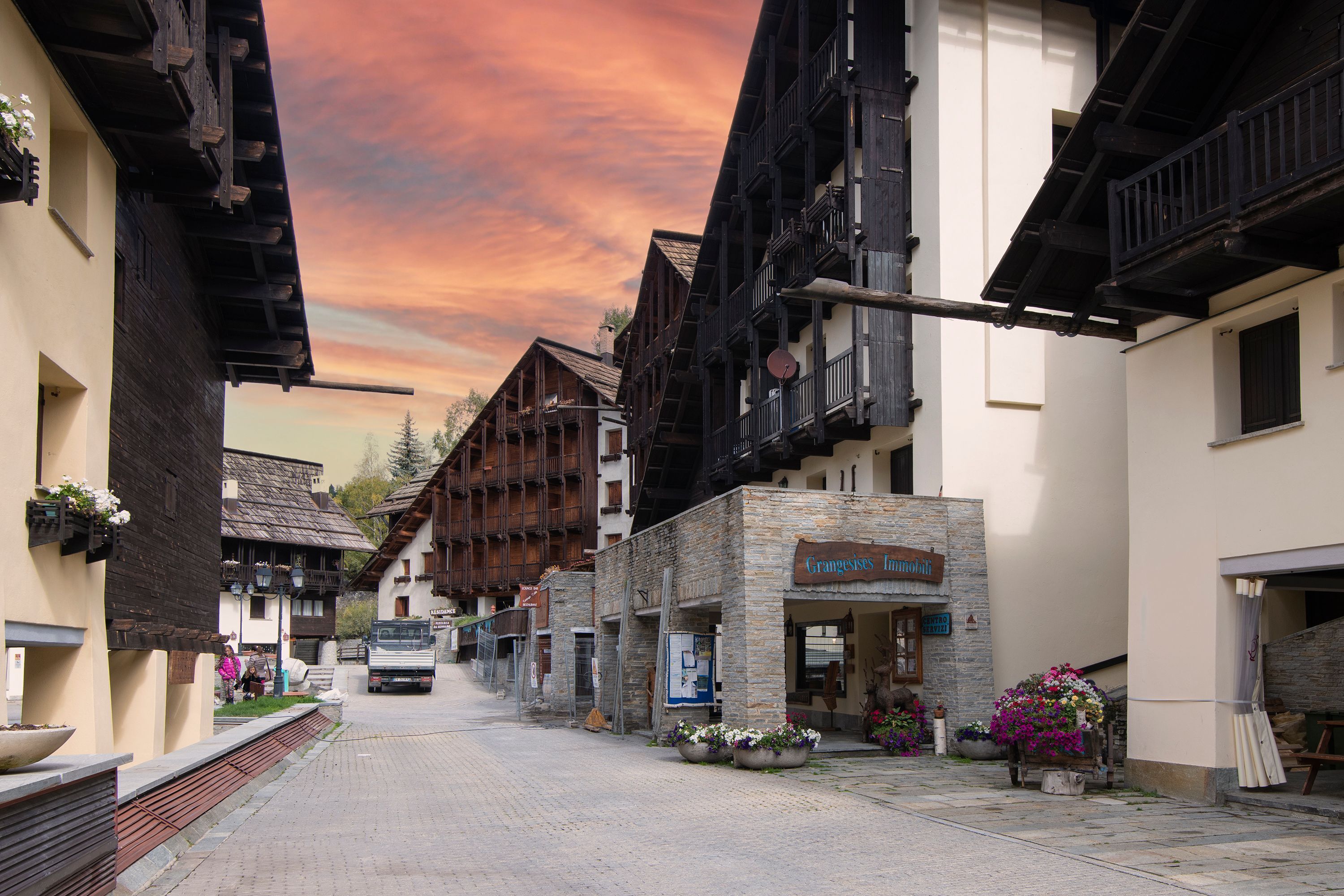 Una strada europea tradizionale con edifici in legno, un edificio in pietra con un cartello e un camion parcheggiato lungo la strada.