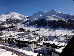 A snow-covered mountain town with modern buildings, ski slopes, and a clear blue sky. - La Stella Alpina in Sestriere (Sestriere)