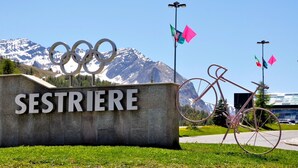 Segnaletica con i cerchi olimpici e la scritta 'SESTRIERE' sullo sfondo delle montagne.
