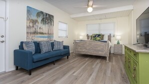 A bedroom with a bed, a blue sofa, a painting, a ceiling fan, and a green dresser.