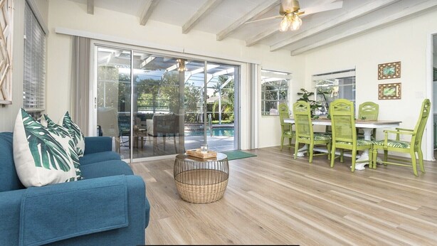 A spacious living area with a blue sofa, a dining table with green chairs, and a ceiling fan.