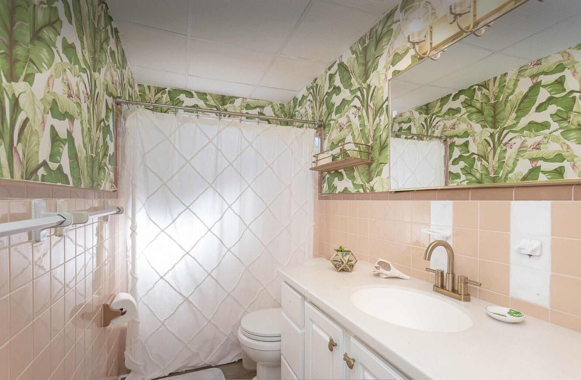 A bathroom with a shower curtain, toilet, sink, and mirror.