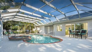 A covered swimming pool with a hot tub, surrounded by a patio area with outdoor furniture and a glass-enclosed structure.