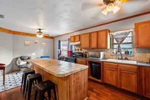 A kitchen with wooden cabinets, a central island with stools, a ceiling fan, and a window with a curtain.