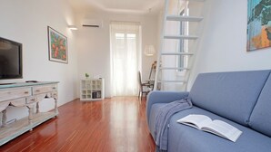 Una sala de estar con sofá, televisión, estantería y ventana con cortinas.