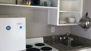 Une cuisine compacte avec des meubles blancs, une cuisinière, un évier et une machine à café posée sur une étagère.