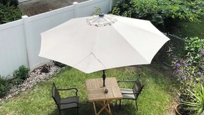 Une petite terrasse avec une table et deux chaises, un parasol et une clôture blanche.