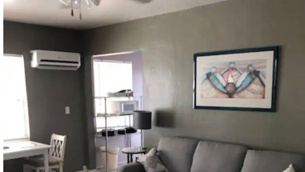 Un salon avec un canapé d’angle gris, un tapis à motifs, un ventilateur de plafond et une œuvre d’art encadrée accrochée au mur.