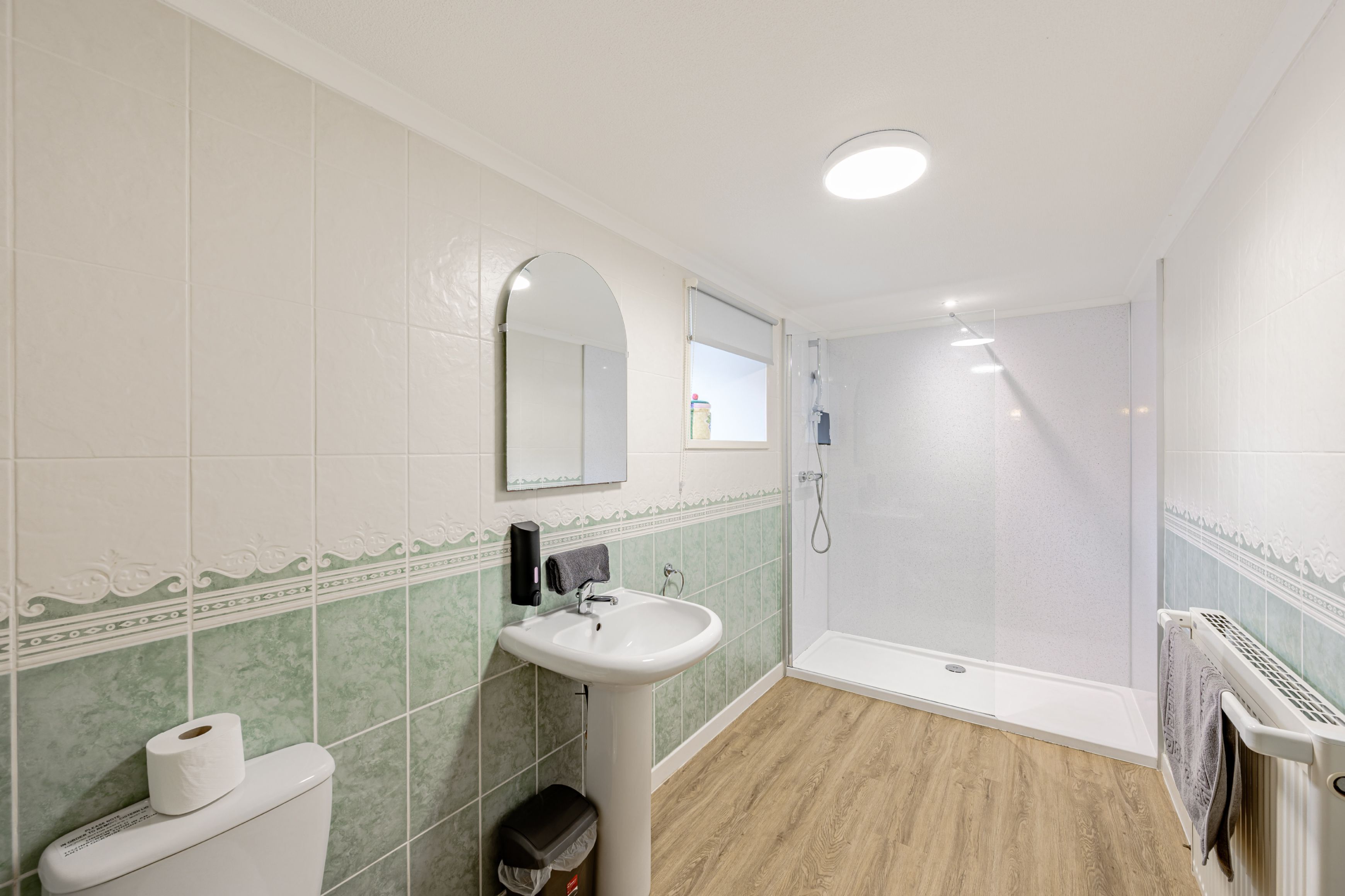 Ein Badezimmer mit Toilette, Waschbecken, Spiegel, Dusche und gefliesten Wänden.