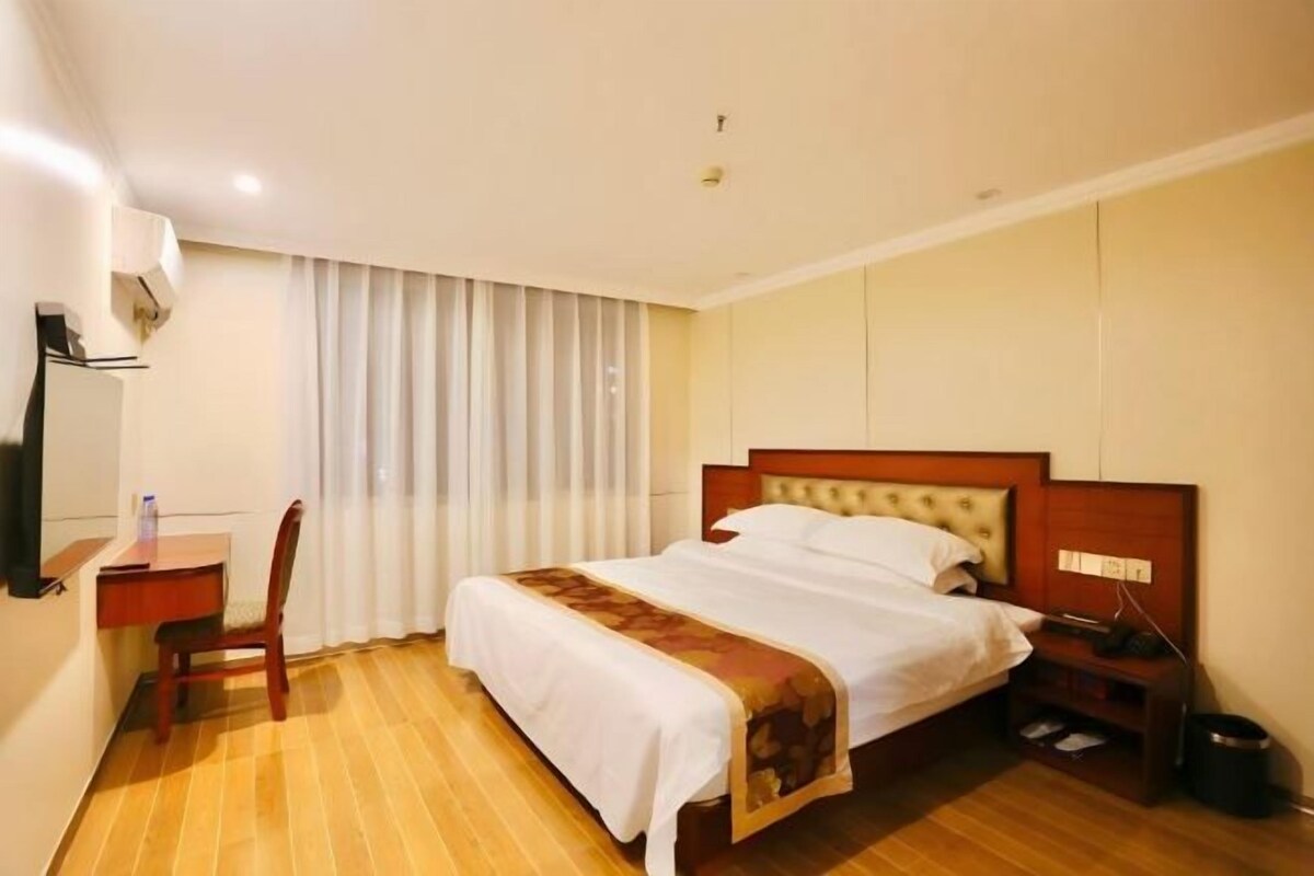 A hotel room with a bed, a desk, a chair, a bedside table, and a trash bin.
