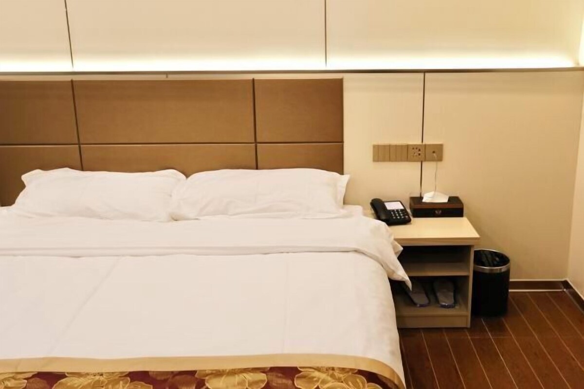 A hotel room with a large bed, a bedside table with a phone and a tissue box, and a trash bin.