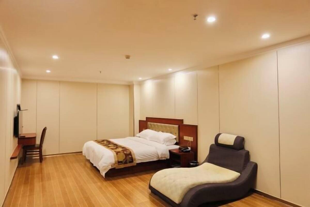 A hotel room with a bed, a bedside table, a chair, and a flat-screen TV.