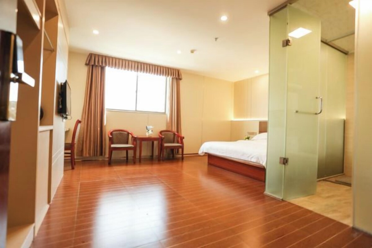 Una habitación de hotel con cama, escritorio, dos sillas, ventana con cortinas y puerta corrediza.