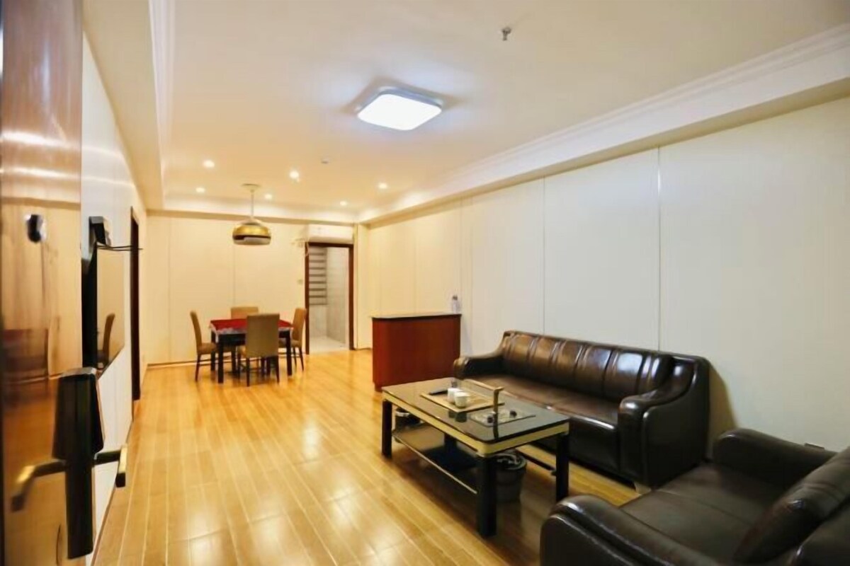 A living room with a leather sofa, a coffee table, a dining area with chairs, and a kitchen area with cabinets.
