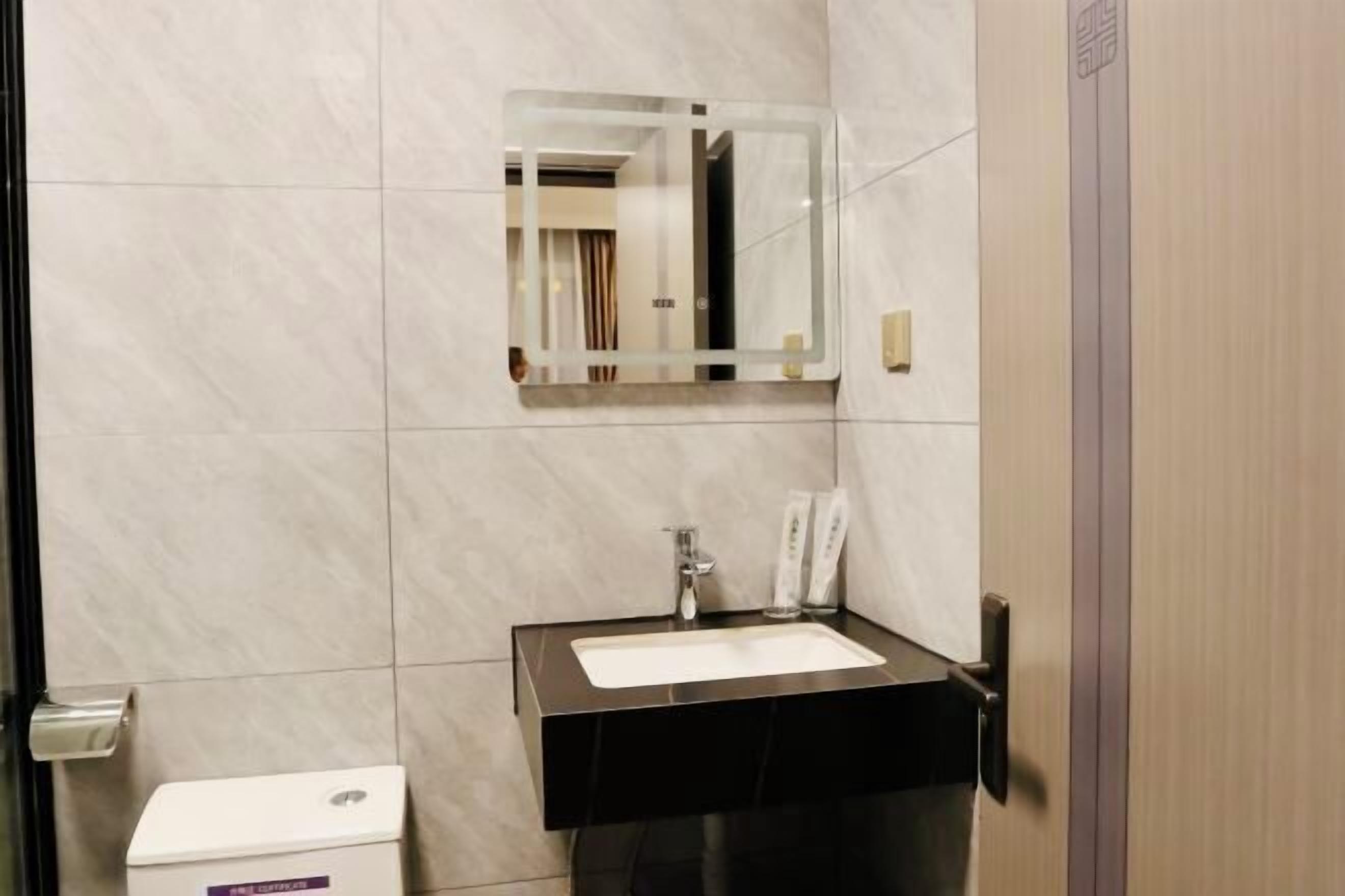 Une salle de bain avec des toilettes blanches, un lavabo noir avec un miroir au-dessus, et un distributeur de serviettes.
