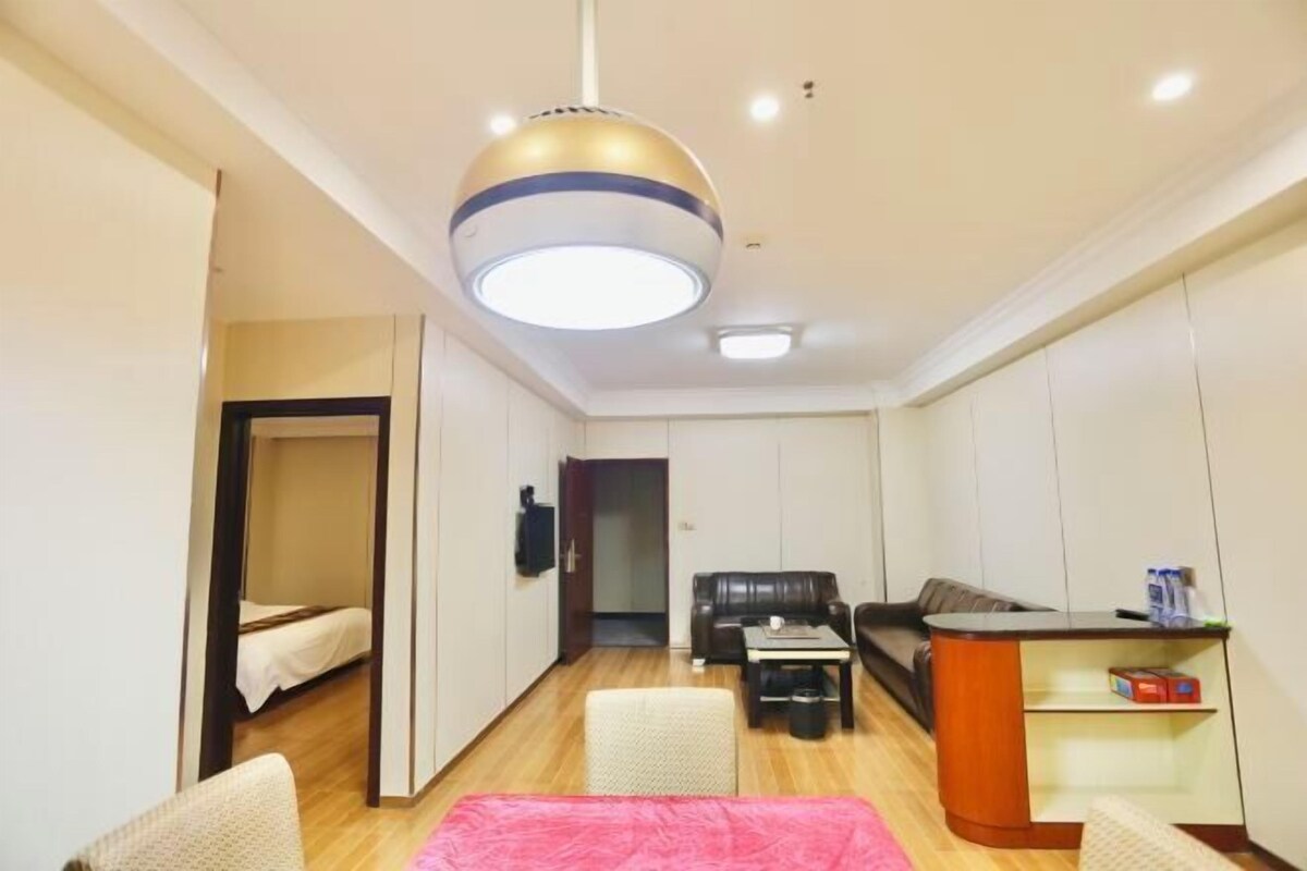 A compact living space with a bed, a sofa, a coffee table, a desk, and a hanging light fixture.