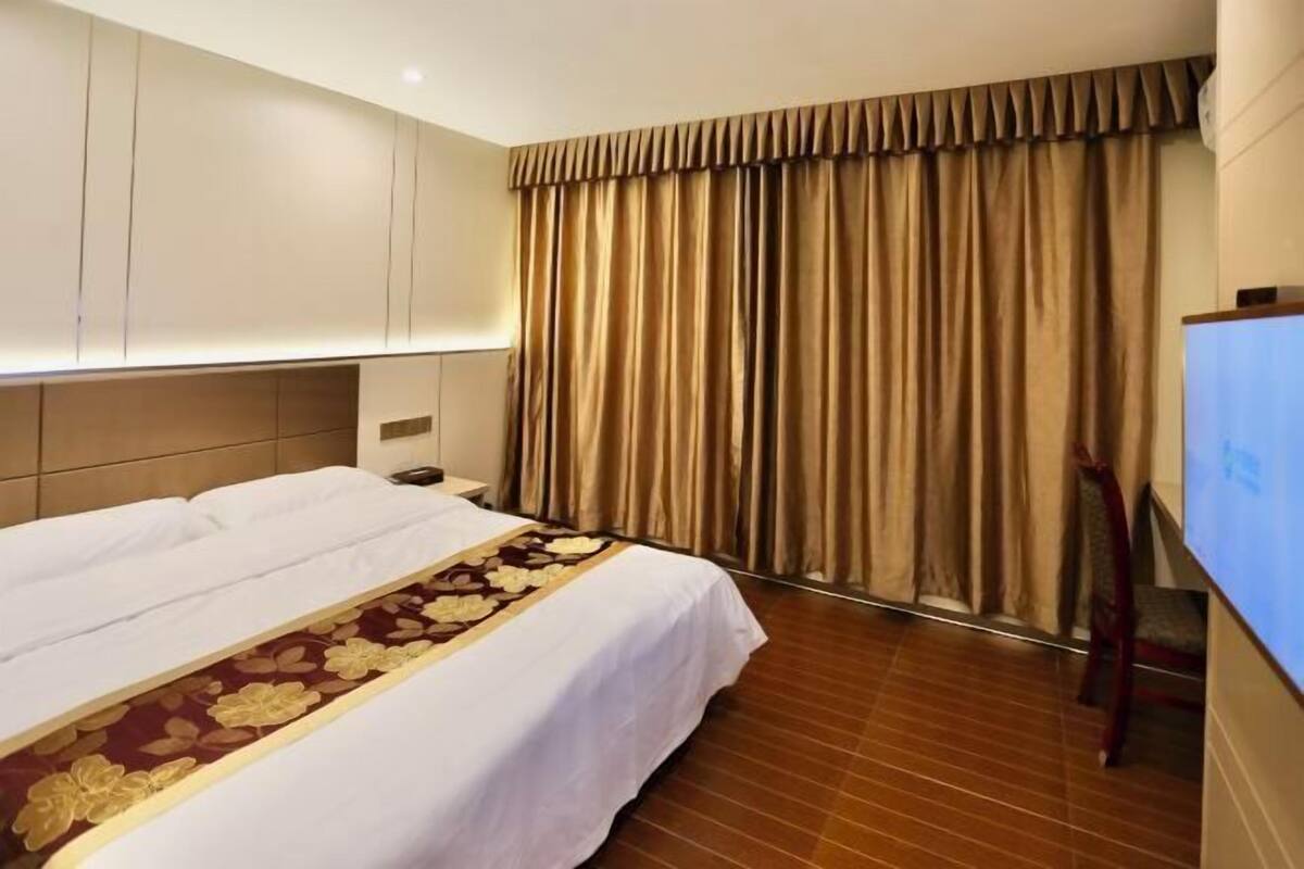 A hotel room with a bed, curtains, a TV, and a wooden floor.