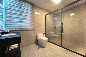 A modern bathroom with a toilet, a glass shower enclosure, and a vanity with a towel rack. - Xinghe Business Hotel (Luhe)