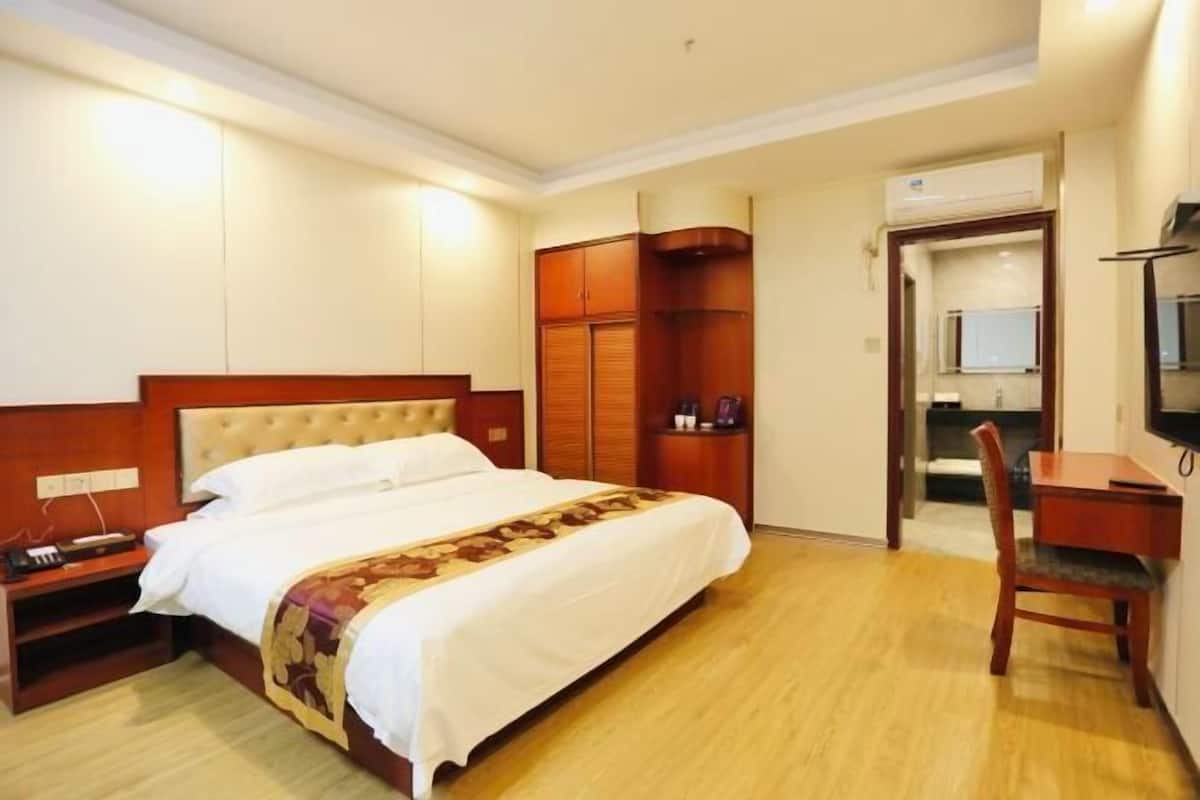 A hotel room with a bed, a desk, a chair, a wardrobe, and an air conditioning unit.